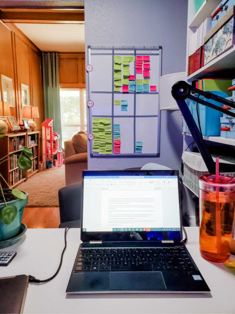 laptop on desk with kanban board on wall in background