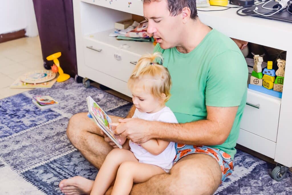 father sitting on floor reading to todder girl