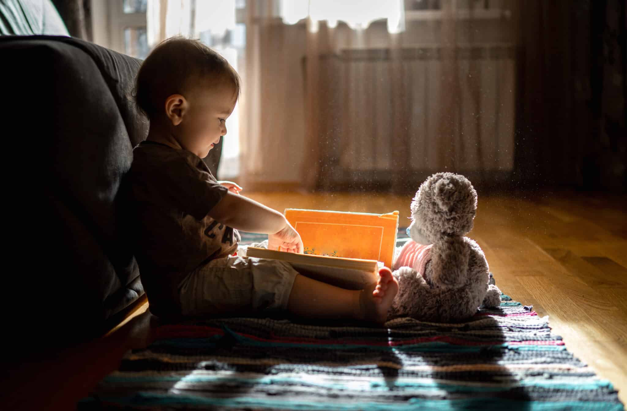 toddler with board book and teddy bear